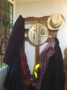 A view of coats and a sunhat on the hall stand with the circular mirror in the centre reflecting the door and stained glass window panel.  