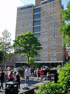 A photograph of the sixteen storey tower Joe lived in as a student, taken on a sunny day with lots of young people in the foreground.