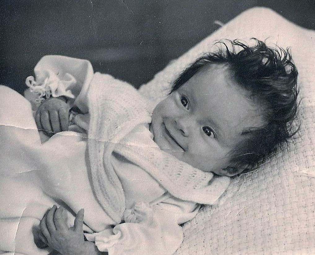 Lindy's black and white photograph of herself as a baby. She has lots of curly hair and a lovely smile.