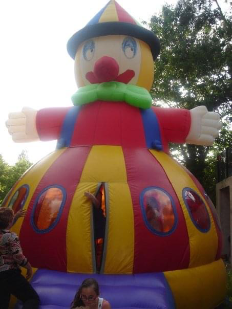 A bouncy castle in the shape of a clown, with children going in and out and waving through the windows.