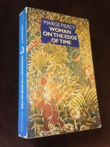 Cover of Marge Piercy's Woman on the Edge of time published by the Women's Press. The cover shows a seated black woman amidst tropical plants, with a butterfly on the bottom right hand corner. 