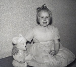 A photograph of Margaret as a child with a ribbon in her hair, wearing a party dress with her arm round her seated teddy bear