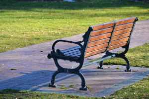 A wrought iron park bench with a wooden seat, next to a path alongside a mowed lawn