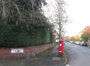 The red post box at the junction of Hartington Road and Corkland Road, Chorlton, with the sun shining on the Autumnal trees