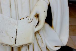 A detail of a white marble statue showing a hand holding an open book.