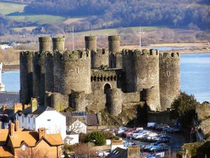 A view of the many round turrets of Conway castle with the estuary and hills behind.  It is a sunny day and the water is blue.