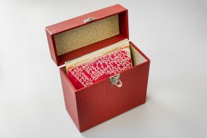 The red-checked singles case is open to show the records inside, all in paper sleeves.  The singles case is like a stiffened box with a clasp fastener.   