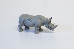 A side view of a grey plastic toy rhino, with its two prominent horns and large sticking up ears.  
