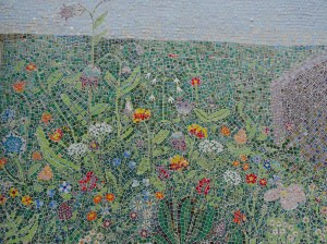 The many wild flowers are yellows, reds, blues, white and purple against a background of various shades of green leaves and grass.