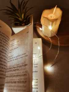 The pages of an open book of poetry, lit from behind by a candle on a table.