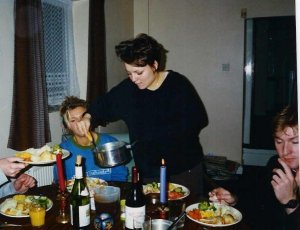 Jolene serving out a roast dinner to three friends seated round a table.  There are candles and bottles of wind on the table. 
