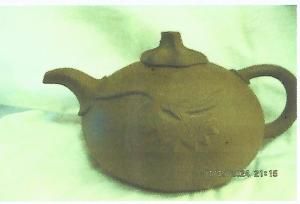 A photo of the small, round, unglazed brown teapot with  its lid and leaves.  