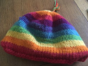 A knitted hat with stripes in the colours of a rainbow. 