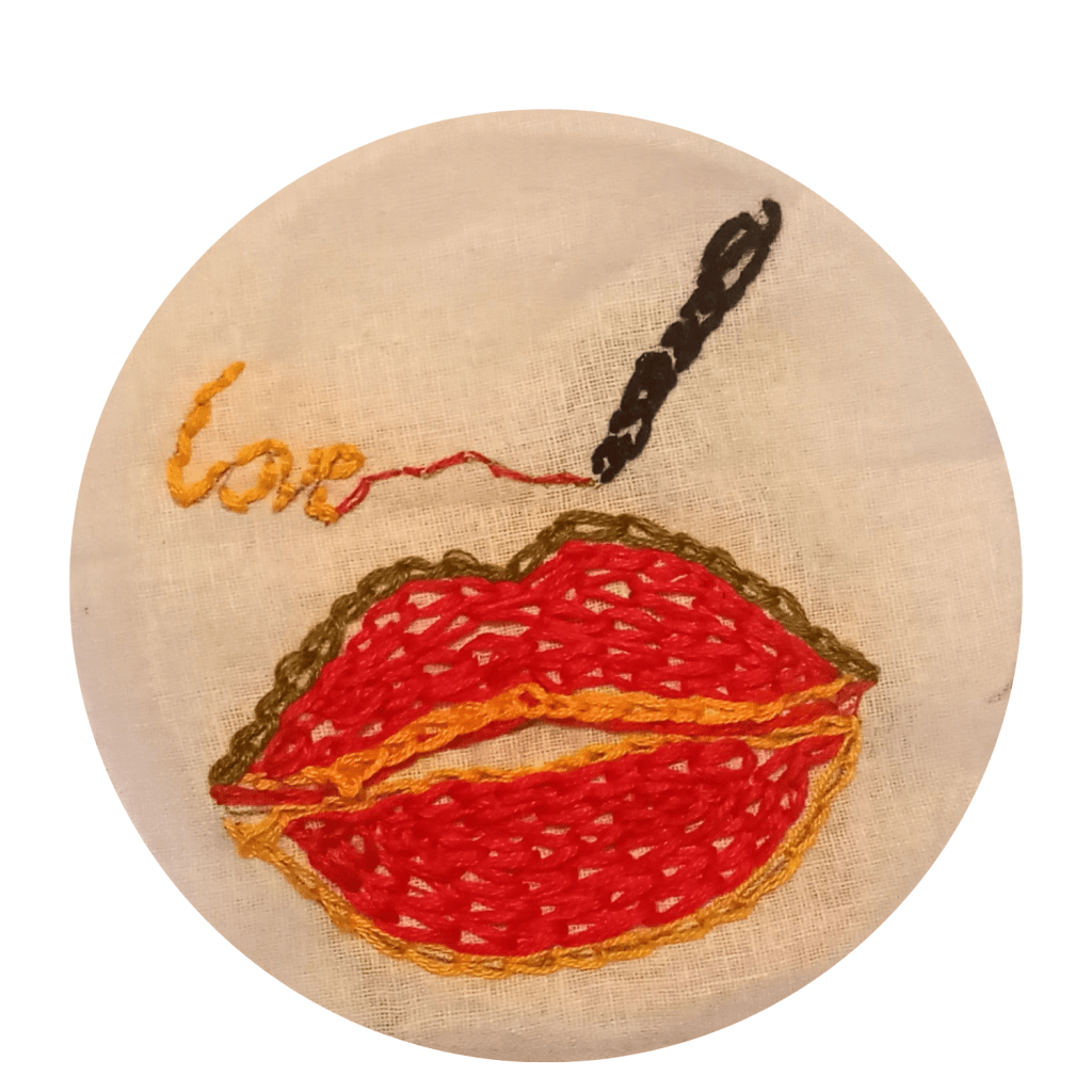 A pair of smiling lips embroidered in red, green and gold (the colours of the Jamaican flag).   Above the lips, an embroidered  black pen is writing the word "love" in gold and red thread. 