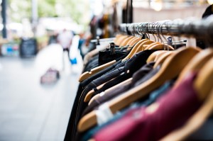 Close-up of clothing on wooden hangers displayed on a metal rack in an outdoor market or shop, with a blurred background showing people and a pedestrian street.