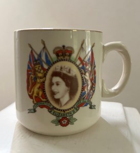 A photograph of a child's coronation mug with the text "The Coronation of Elizabeth II June 2nd 1953" displayed on a green ribbon underneath a photograph of the Queen on the Royal Crest