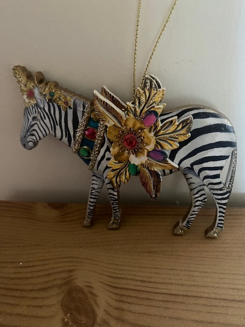 Image description: A zebra on a gold chain, decorated with gold leaves and jeweled flowers on its head and around the saddle.  