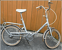 Image description: A bicycle with small wheels, extended "sit up and beg" style handlebars and a high saddle.  There is a rack on the back to attach a bag, hence the name "shopper" bike.