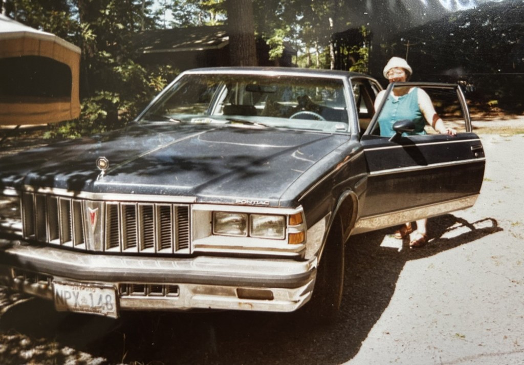 Image description: Margaret behind the open door on the driver's side of the older Pontiac.